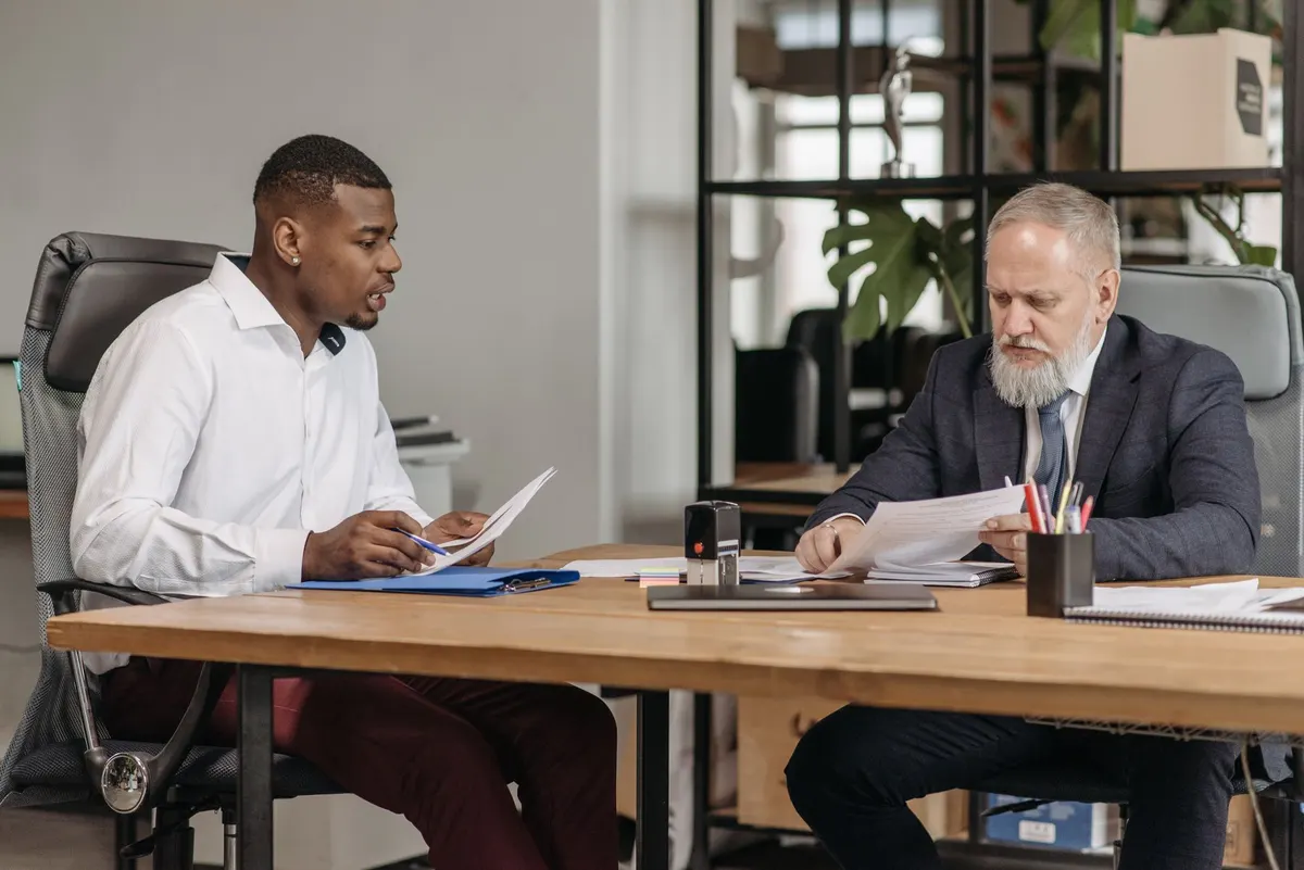Two men at a wooden desk reviewing papers during a meeting