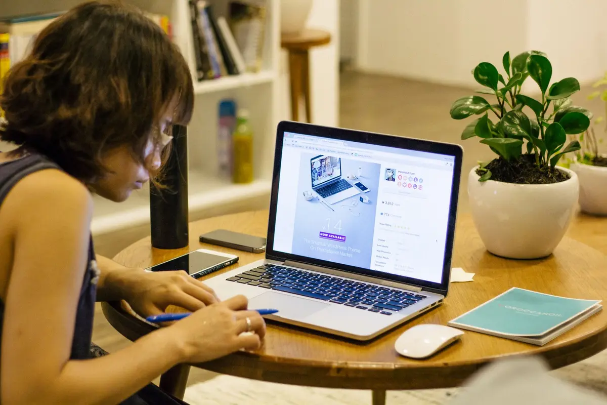 Woman working remotely from home with a laptop, pen, and plant on her desk.