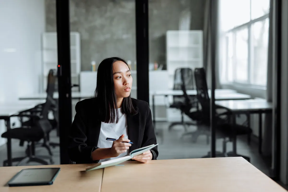 A woman at a desk looking off to the side, pen in hand, thinking something over