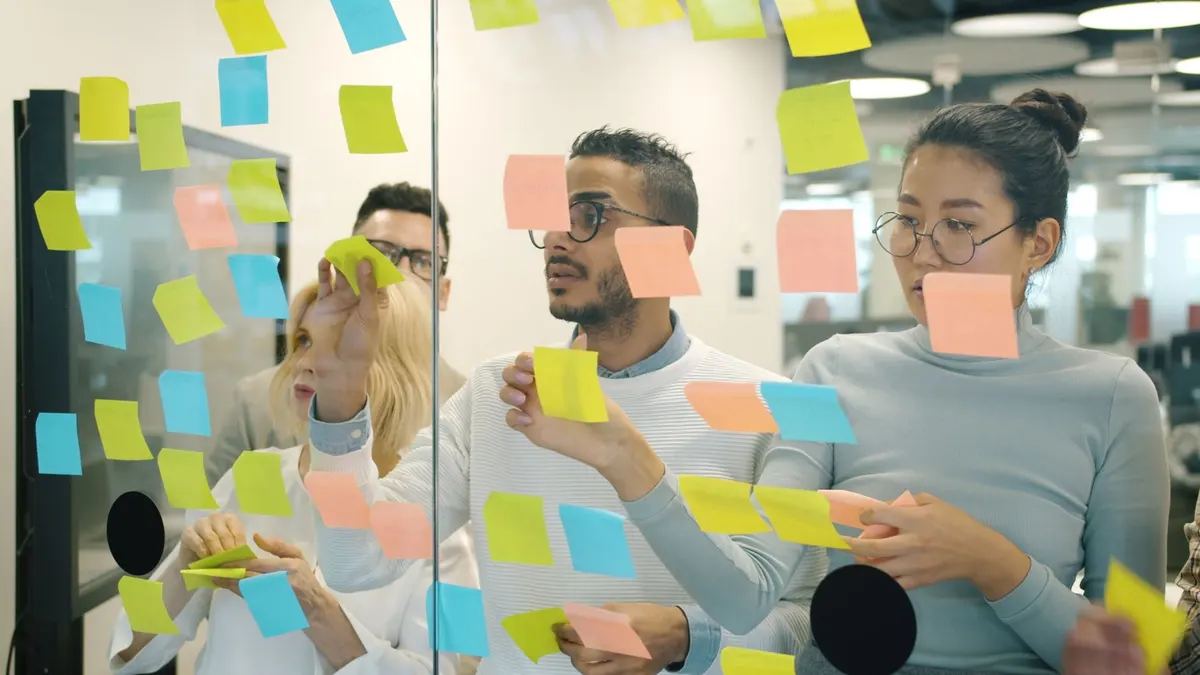 Several colleagues placing sticky notes on a glass wall while planning together
