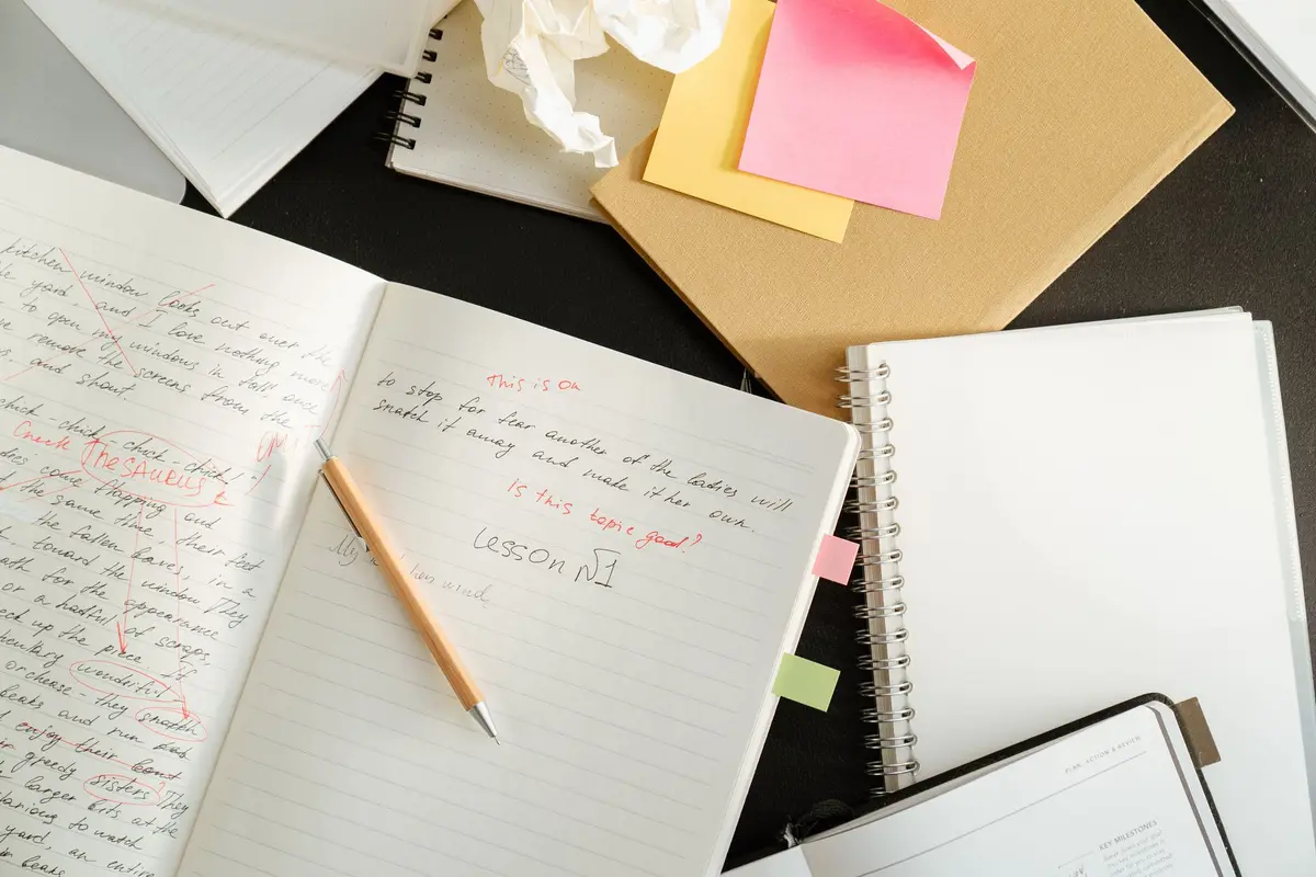 A cluttered desk with notebooks, sticky notes, and stationery for educational purposes.