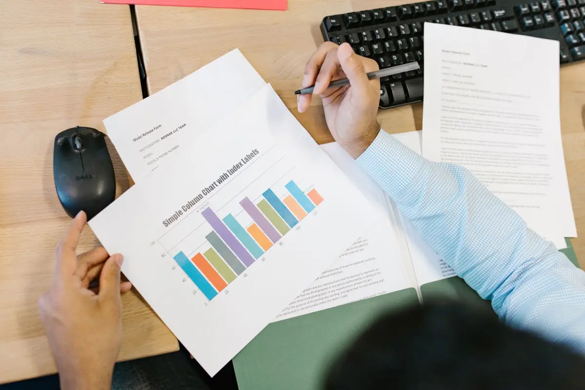 A business analyst reviews a colorful bar chart and documents at a desk.