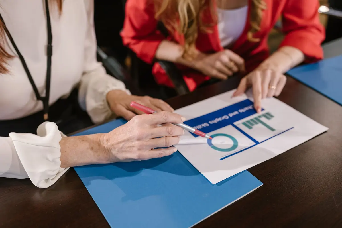 Two women analyzing business charts and reports during a meeting at a wooden table.