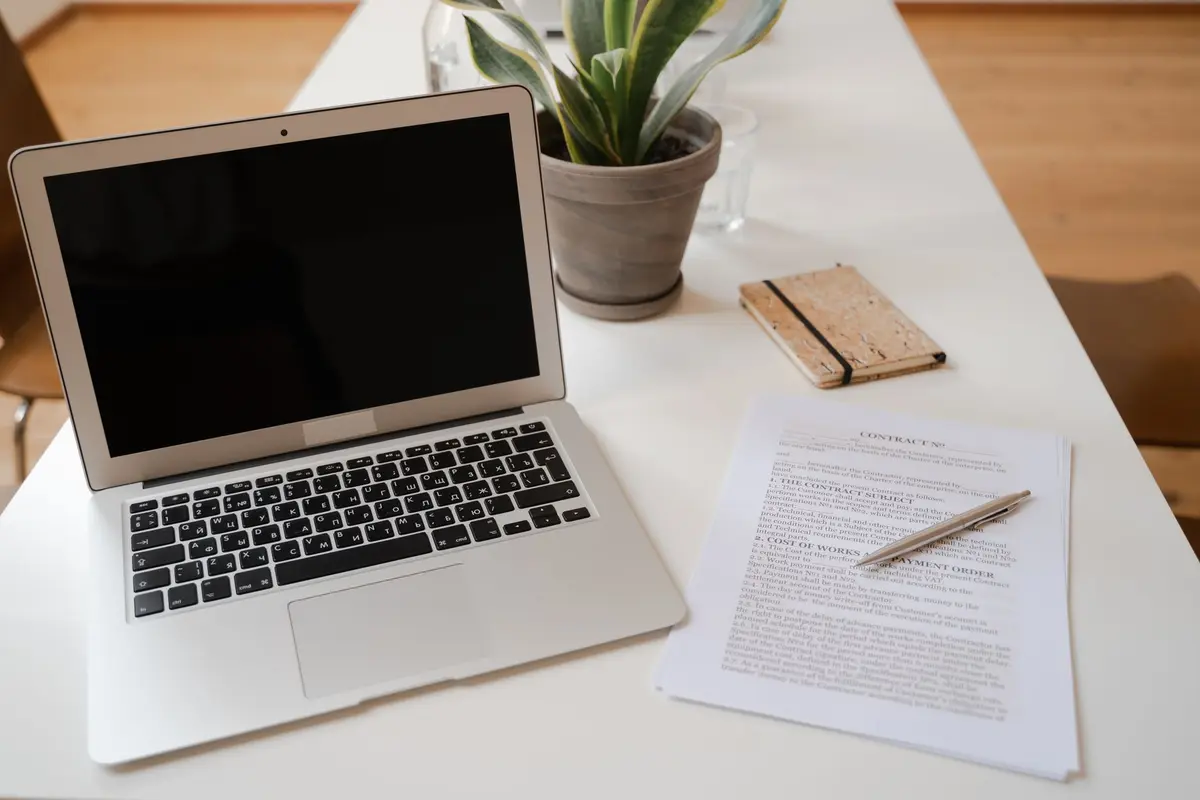 A serene office desk setup featuring a laptop, plant, and contract document.