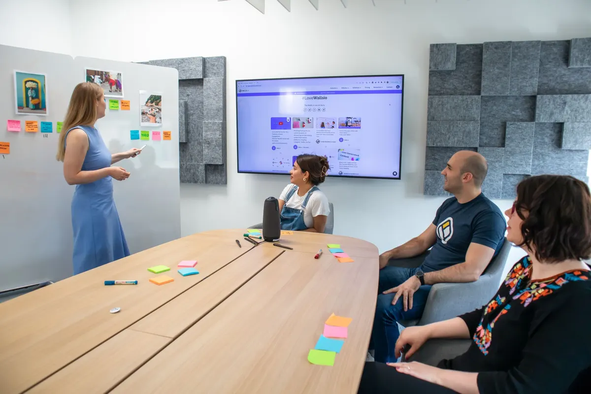 A woman standing at a whiteboard in a meeting room while colleagues sit at a long table